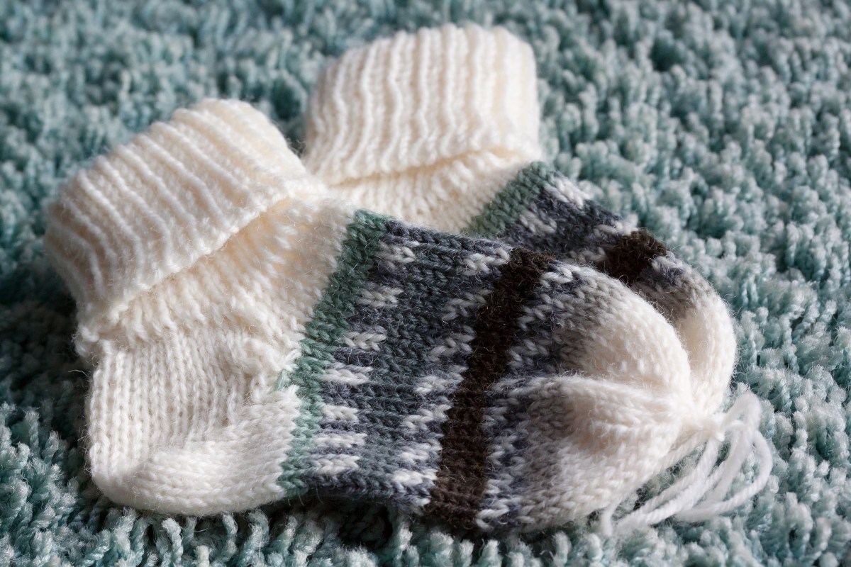 Hand knit baby socks, cream with a blue, green and brown striped section, on a blue rug.
